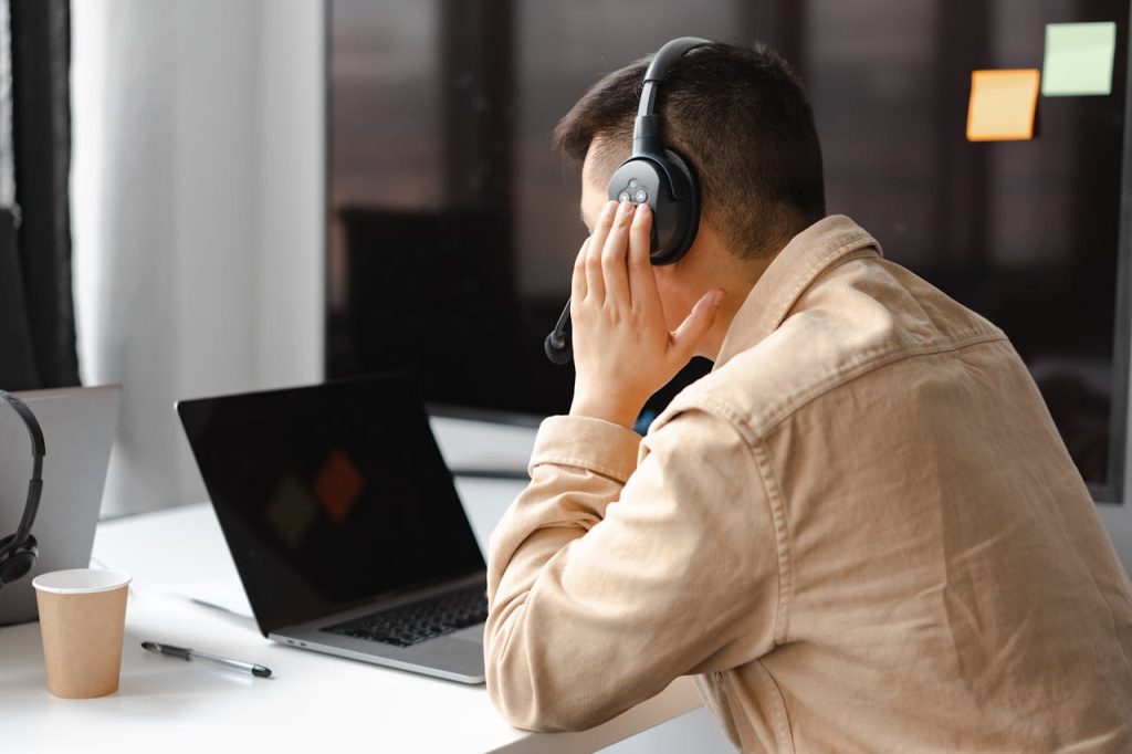 man-wearing-his-headphone-in-front-of-his-laptop-7681302 A man wearing headphones works at a laptop in a modern office setting.