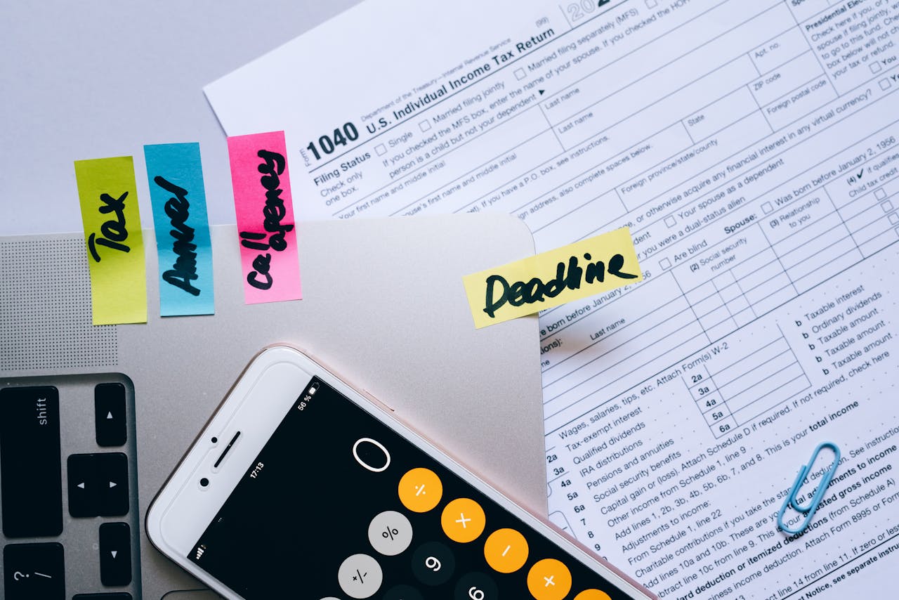 why-choose-me-01 Office desk flat lay showing tax documents, calculator app on smartphone, sticky notes, and paperclips.